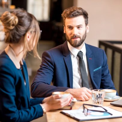 man with beard speaking to women with book and glasses on table