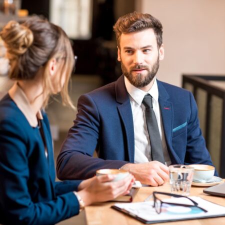 man with beard speaking to women with book and glasses on table